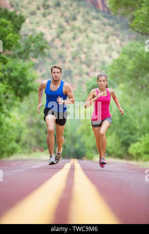 L'exécution de young mixed race woman sprint concentrés sur route à l'extérieur dans la nature de l'exercice jogging sport. Joli modèle asiatique et caucasienne modèle masculin. Banque D'Images