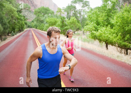 Porteur de la formation - jeune couple multiracial exécutant l'exercice concentré sur route dans une nature magnifique. Fitness homme modèle caucasien contrôle de temps ou impulsion de moniteur de fréquence cardiaque montre. Banque D'Images