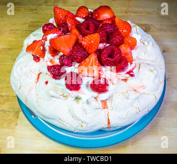 Libre d'une pavlova fraîchement cuits - un dessert à base de meringue garnie de crème, fraises et framboises, reposant sur une plaque sur une table. Banque D'Images