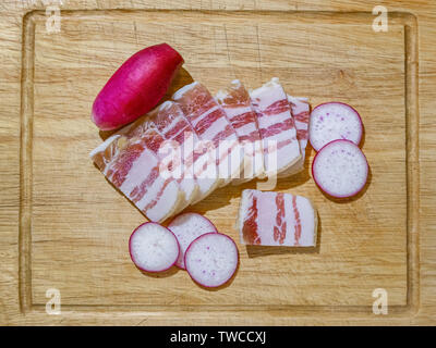 Morceaux de fines tranches de bacon congelé avec des couches de viande et le radis disposés sur une cuisine en bois. Snack-russo-ukrainiens traditionnels appétissants Banque D'Images
