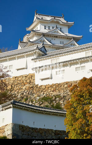 Le château de Himeji en haut de murs de pierre fortifiée dans la lumière de l'après-midi chaud. Banque D'Images