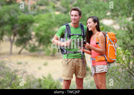 Tablet computer - couple hiking en utilisant internet et ordinateur tablette pc guide book app sur la randonnée dans le parc national de Zion. Randonneur actif interracial couple, femme asiatique, caucasian man trekking dans l'Utah, USA. Banque D'Images