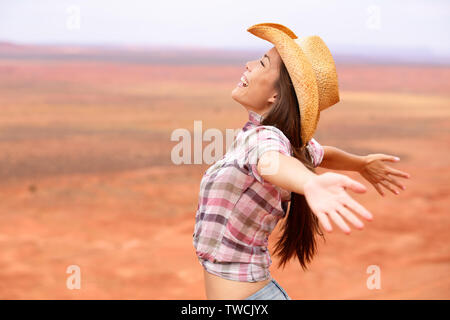 Cowgirl - femme heureux et libres sur american prairie wearing cowboy hat avec bras tendus dans la liberté concept. Beautiful smiling Caucasian multiraciale Asian young woman outdoors, Arizona, Utah, USA. Banque D'Images