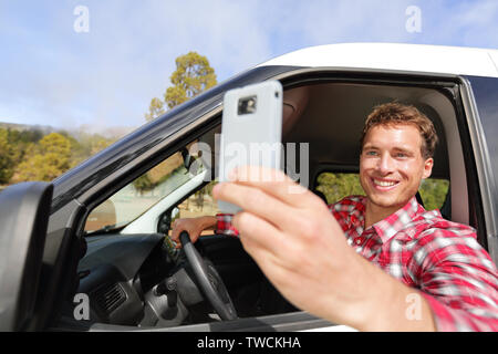 Photo prise du pilote de l'appareil photo avec la conduite en voiture. smartphone Homme heureux de prendre photo avec smart téléphone appareil hors de la fenêtre de voiture pendant le voyage par la route de voyage. Jeune homme de race blanche dans son modèle 20s. Banque D'Images