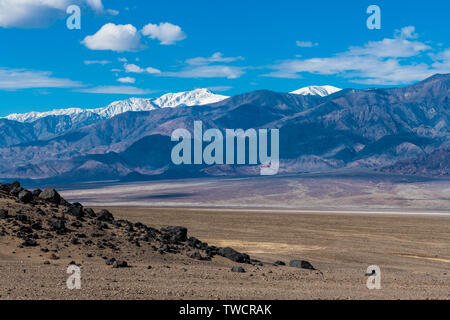 La terre stérile et les roches d'un paysage de désert aride contraste avec les sommets de montagnes enneigées - Panamint Range dans Death Valley National Park Banque D'Images