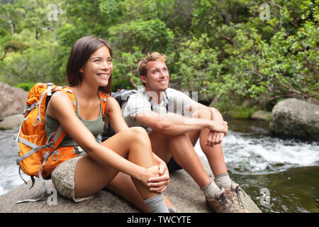 Couple de randonneurs par river bénéficiant d'activité extérieure portant des sacs à dos en s'asseyant. La femme et l'homme hiker à sourire avec plaisir. Image Style de vie sain. Banque D'Images