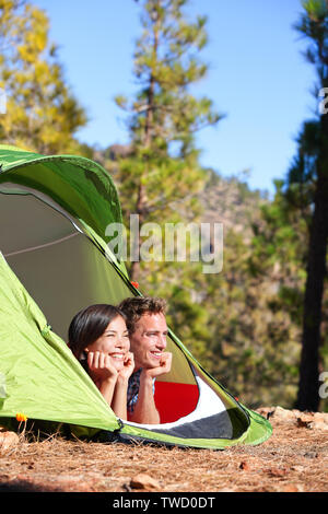 Couple camping en tente à la romantique à voir en forêt. Les campeurs smiling happy en plein air dans la forêt. Couple multiracial relaxant après activité de plein air. Asian Woman, man. Banque D'Images