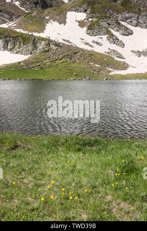 Vue sur le lac de rein, grand groupe lointain de randonneurs de grimper la colline couverte de neige sur une piste de fameux sept lacs de Rila Banque D'Images