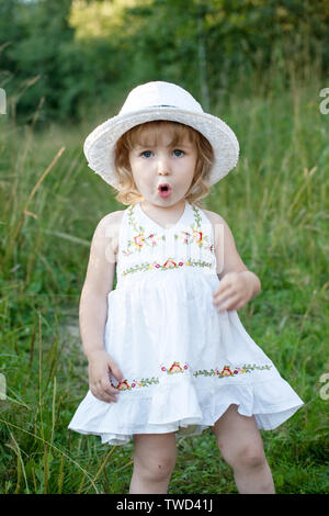 Petite fille en robe et chapeau blanc sur fond de prairie d'été permanent vue rapprochée Banque D'Images