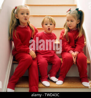 Trois enfants assis sur un escalier qui portaient tous des pyjama rouge Banque D'Images