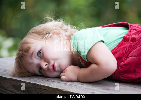 Cute pensive kid girl lying on outdoor banc en bois Banque D'Images