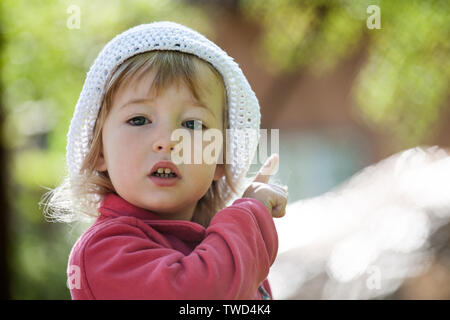 Petit enfant caucasian girl in white hat pointing with index vue rapprochée Banque D'Images