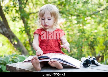 Kid girl sitting avec gros livre sur fond de plein air d'été Banque D'Images