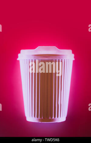 Close up de café tasse pour aller dans la lumière au néon lumineux sur fond rose. Eco concept. Place pour le texte. Banque D'Images