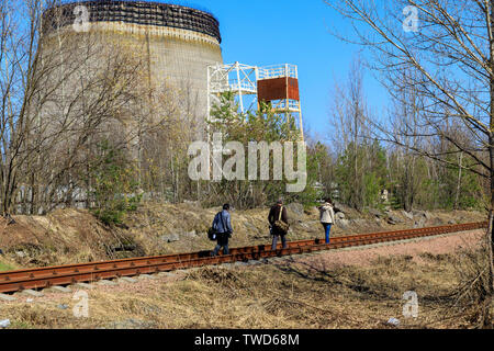 L'Europe de l'Est, l'Ukraine, Pripyat, Tchernobyl. Les touristes à marcher le long des voies ferrées près de la tour de refroidissement non fini pour les réacteurs 5 et 6 qui ont été nev Banque D'Images