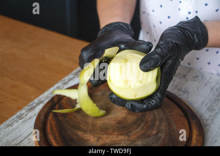Femmes en noir gants peel off une pomme verte sur une planche en bois, selective focus, copyspace Banque D'Images