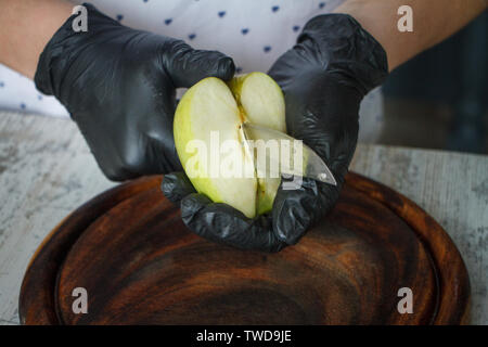 Femmes en noir gants coupe une pomme verte sur une planche en bois, selective focus, copyspace Banque D'Images