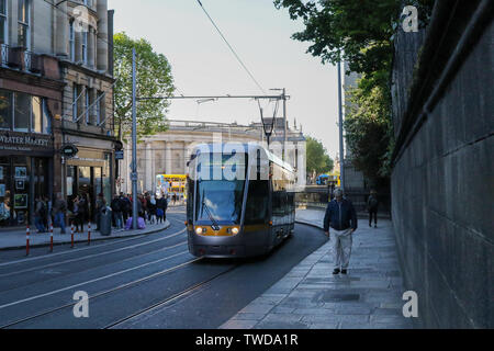 Homme marchant le long de la chaussée de la rue de Dublin comme tramway Luas passe par beau soir d'été avec des gens qui marchent à la maison du travail au soleil sur Nassau St. Banque D'Images