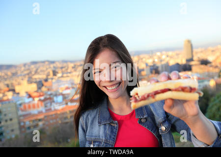 Jamon Serrano Sandwich. Woman eating à Barcelone, Espagne montrant espagnole traditionnelle, guéri jambon ibérique. Se concentrer sur la fille, Barcelona skyline en arrière-plan. Banque D'Images