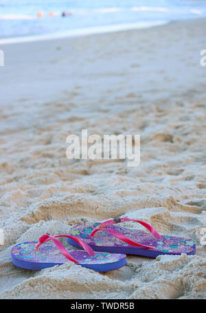 Vertical image d'une paire de rose et violet sandales tongs sur la plage de sable Banque D'Images