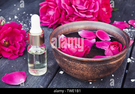 Près de l'huile essentielle de pétales de rose rouge bol avec sur un fond en bois sombre. L'aromathérapie. Banque D'Images