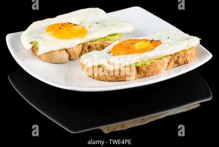 Toasts avocat surmontée d'oeufs au plat avec réflexion isolé sur fond noir. Studio Shot Banque D'Images