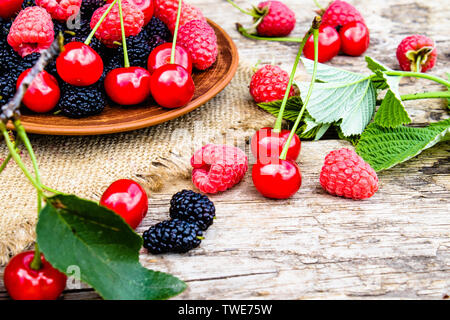 Fruits des framboises, cerises, mûres dans un bol sur fond de bois et de toile. Close-up Banque D'Images