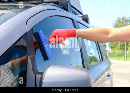 Un homme avec un racloir en caoutchouc supprime le reste de l'eau du verre après avoir laver la voiture. Lavage de voiture. Lave-linge en libre-service complexe. C haute pression Banque D'Images