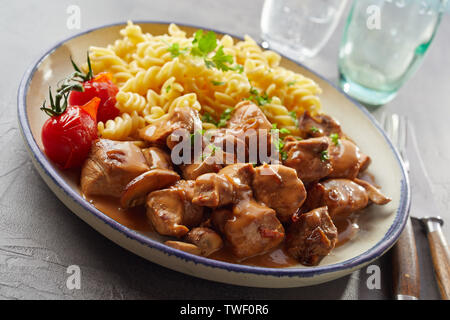 L'angle plan rapproché sur bol de délicieux pâtes fusilli, tomates et morceaux de porc assaisonné de sauce Banque D'Images