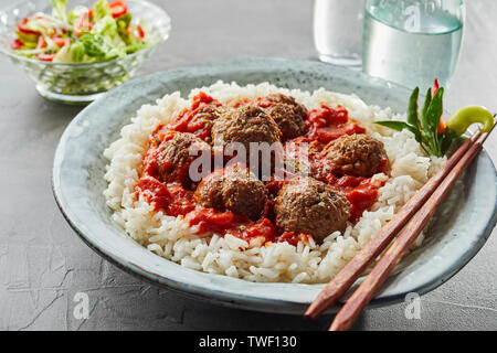 Riz frit délicieux avec des boulettes de viande et la sauce dans un bol blanc près de verre d'eau et un petit bol holding vegetables Banque D'Images