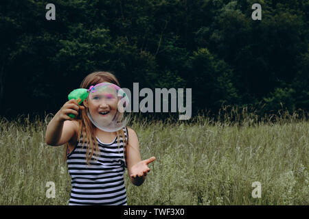 Girl blowing bubbles avec canon à bulles. Jeune enfant jouer dehors. Activités de jour d'été. Heureux, joyeux enfant à l'extérieur. Avoir du plaisir seul. Belle et pittoresque paysage forestier. Paysage pittoresque Banque D'Images