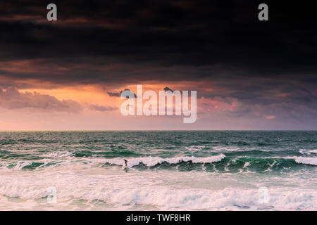 Un coucher de soleil spectaculaire en tant que surfeur solitaire conduit une vague à la plage de Fistral à Newquay en Cornouailles. Banque D'Images