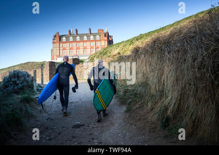 Leur maturité surfers carrying surfboards marcher jusqu'à la pointe à l'hôtel à Newquay Fistral à Cornwall. Banque D'Images