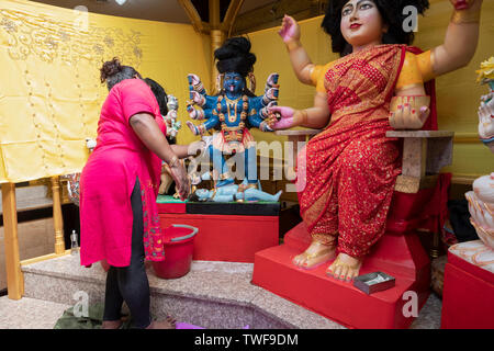 Une pieuse femme hindoue se lave une statue de la déesse Kali avant l'installation de nouveaux faits les vêtements. Dans le Queens, New York. Banque D'Images