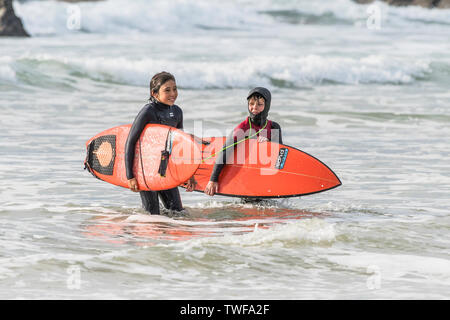 Deux jeunes surfeurs avec leurs planches de Skinpups rouge et sortant de la mer sur la plage de Fistral à Newquay en Cornouailles. Banque D'Images