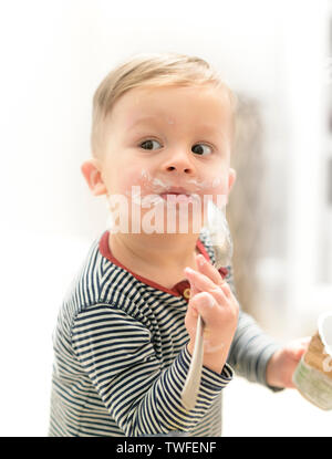 Little Boy eating yoghurt avec soif, avoir un drôle de visage malpropre Banque D'Images