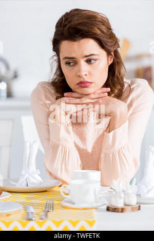Triste belle femme assise avec les doigts entrelacés à table Banque D'Images