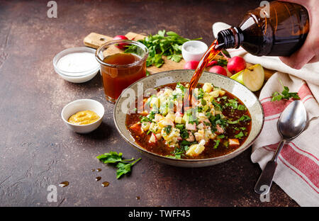 Soupe froide Okroshka russe avec des saucisses, des légumes et de kvas bol et ingrédients sur le tableau noir Banque D'Images