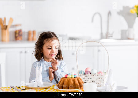 Cute kid assis à table et à la brioche de Pâques à oeufs peints et dans la cuisine Banque D'Images