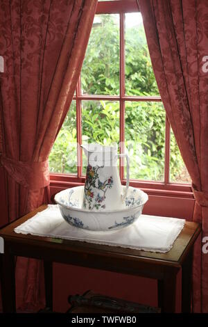 Céramique pichet victorien de l'eau et le bol sur une table devant la fenêtre rideaux prêts à laver tôt le matin Banque D'Images