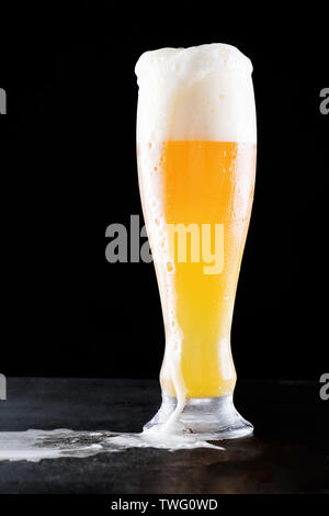 Artisanat à froid de la lager légère de la bière dans un verre avec de l'eau débordante chute avec l'écoulement de la mousse et belle bière renversé sur un fond noir avec reflectio Banque D'Images