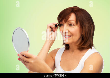 Smiling senior woman with mirror le mascara Banque D'Images