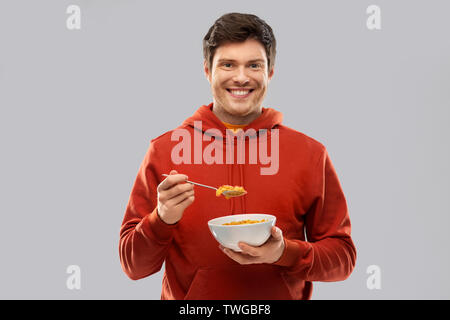 Smiling young man in red hoodie de manger les céréales Banque D'Images