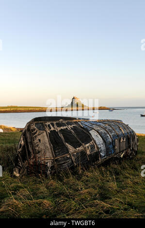 Un vieux bateau de pêche tourné à l'envers et utilisé comme une cabane de stockage de bateau sur la plage de Lindisfarne Holy Island avec Lindisfarne Castle dans le Banque D'Images