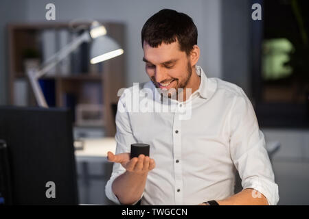 Businessman using smart speaker à office de nuit Banque D'Images