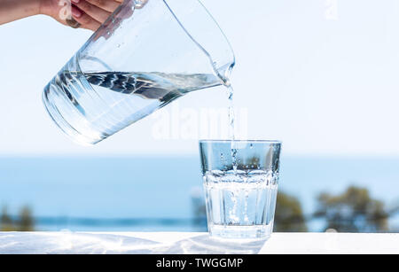 On verse de l'eau purifiée à partir d'une verseuse en verre dans un verre. Le concept d'un mode de vie sain. Banque D'Images