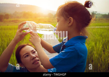 Mère aider ses enfants à l'eau potable de la bouteille en champ de riz. cheveux longs garçon. Galerie d'images haute résolution. Banque D'Images