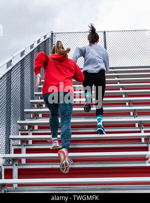 Deux high school track and field runners sont le sprint en rouge des gradins sur un jour nuageux à la pratique. Banque D'Images