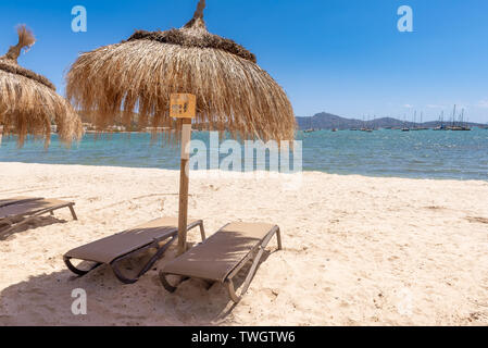 Des parasols de paille avec des chaises longues sur la plage de sable dans la belle ville de Port de Pollença (Puerto Pollença). Mallorca. Espagne Banque D'Images
