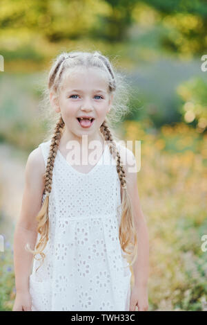 Funny Girl holding tresses de cheveux. Petite fille mignonne avec de longs cheveux blonds montrant la langue à l'extérieur. Kid : exprimer des sentiments. Poisson d'avril Banque D'Images